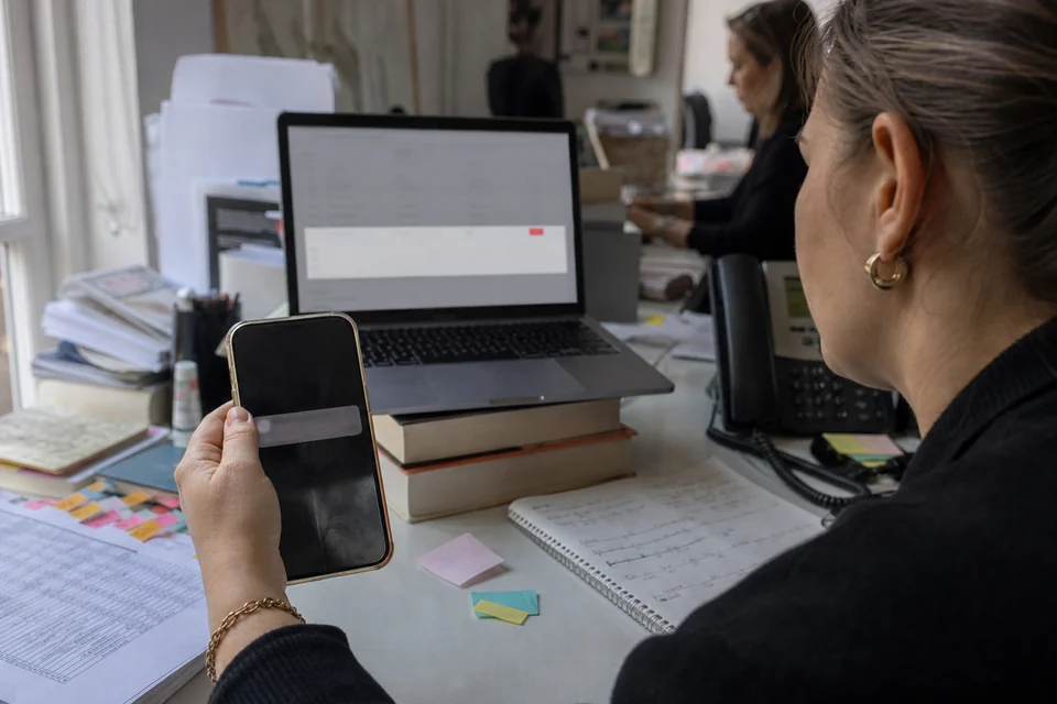 PR manager holding a phone with a lock screen notification, behind it a laptop showing one mention opened in a detail panel with a red tag