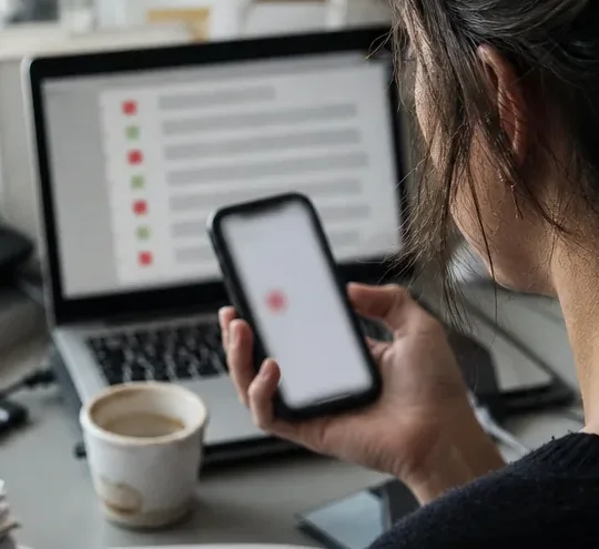 Phone with a fresh mention alert held in front of a laptop feed of mention rows tagged red and green