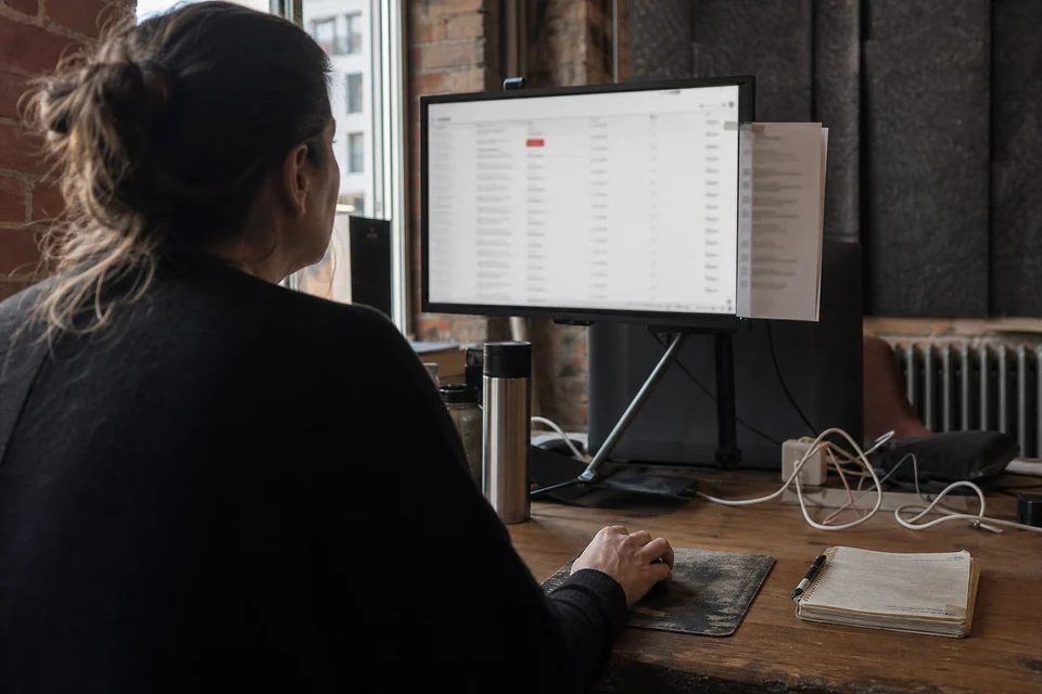 Over the shoulder view of a hand scrolling a long feed of mention rows on a monitor, one row flagged in red